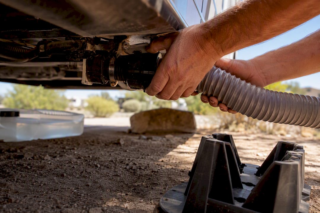 Hands connecting sewer hose to RV sewer outlet